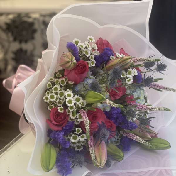 Bouquet of pink roses, lilies, and purple flowers wrapped in white paper