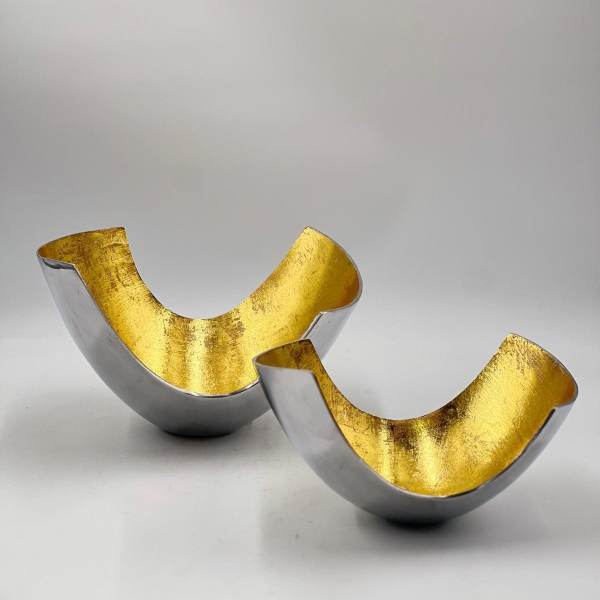 Two metallic gold and silver decorative bowl-shaped objects on a white surface