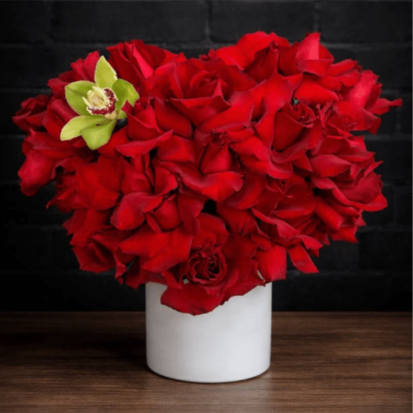 Red rose arrangement in a white vase with a green orchid accent