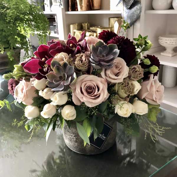 Mixed bouquet of roses, orchids, and succulents in a stone vase
