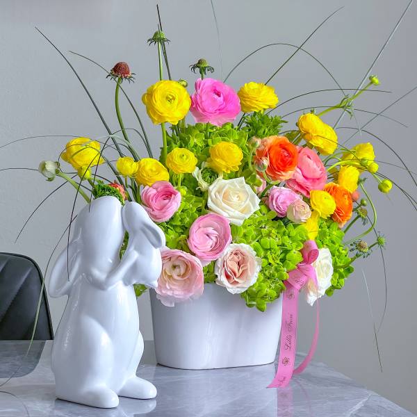 Colorful flower arrangement in a white vase beside a white rabbit figurine