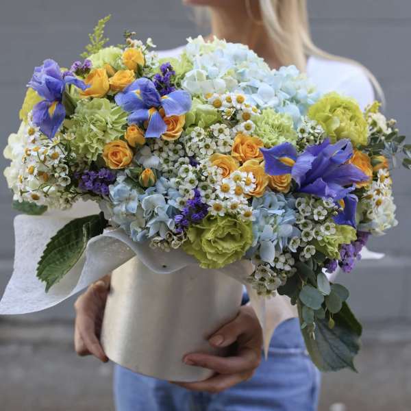 Large bouquet of blue, yellow, and green flowers wrapped in white paper