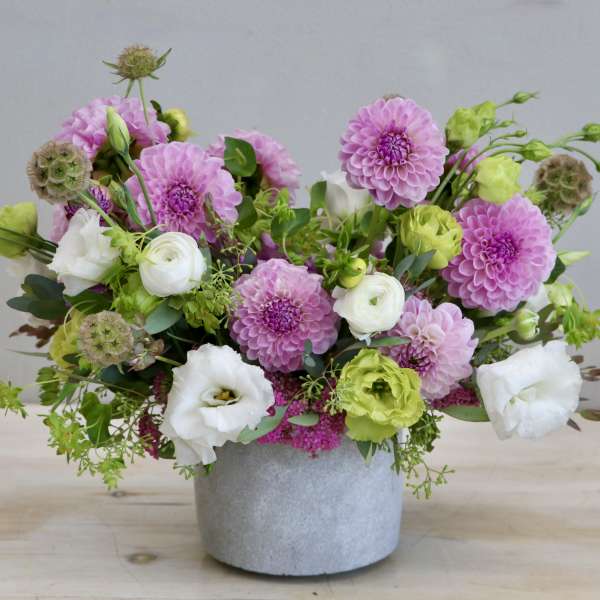 Low arrangement of pink dahlias with white and green blooms in a gray pot.