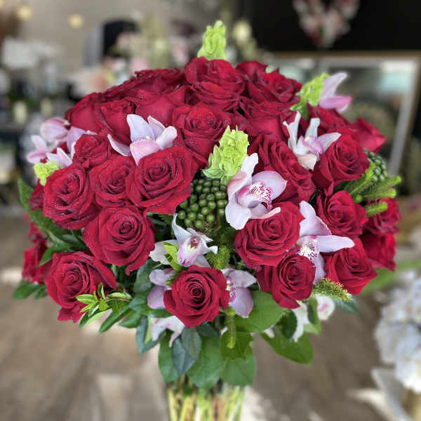 Bouquet of red roses with pale pink orchids in a clear glass vase