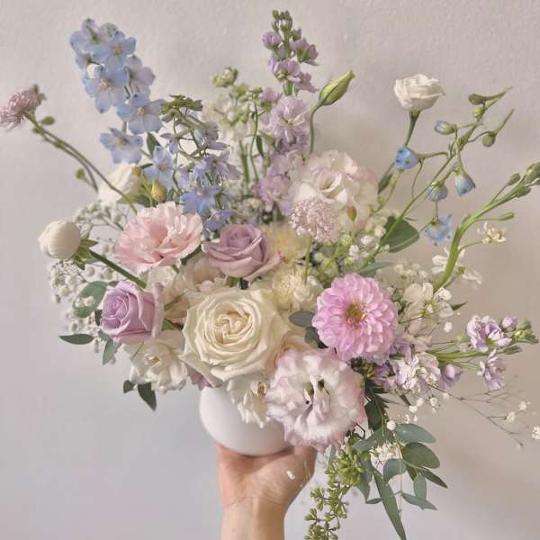 Pastel bouquet of roses, lisianthus, and blue delphinium in a white vase