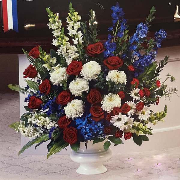 Large red, white, and blue floral arrangement in a white pedestal vase