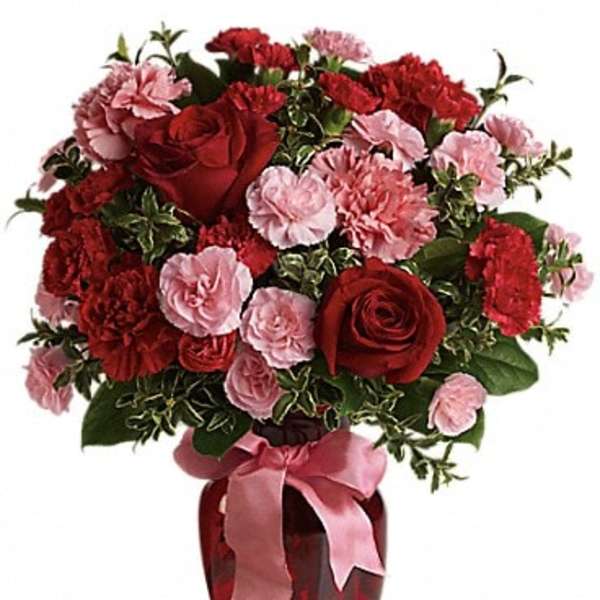 Red roses and pink carnations in a red vase with a pink ribbon
