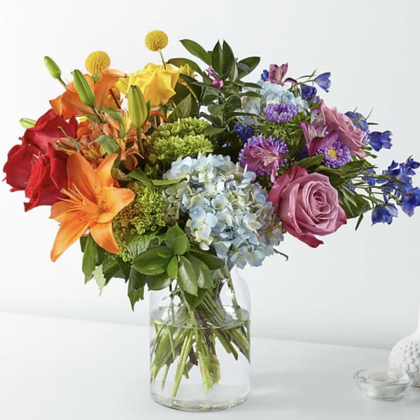 Mixed bouquet of roses, lilies, hydrangeas, and other flowers in a glass vase