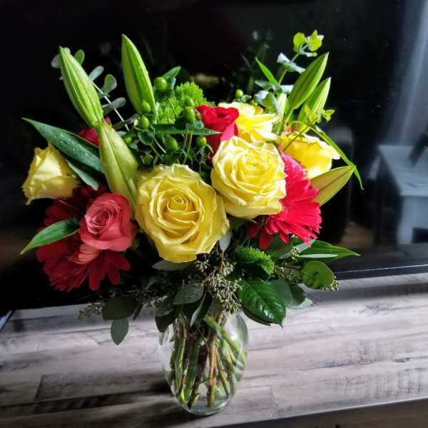 Bouquet of yellow and red roses with lilies in a clear glass vase