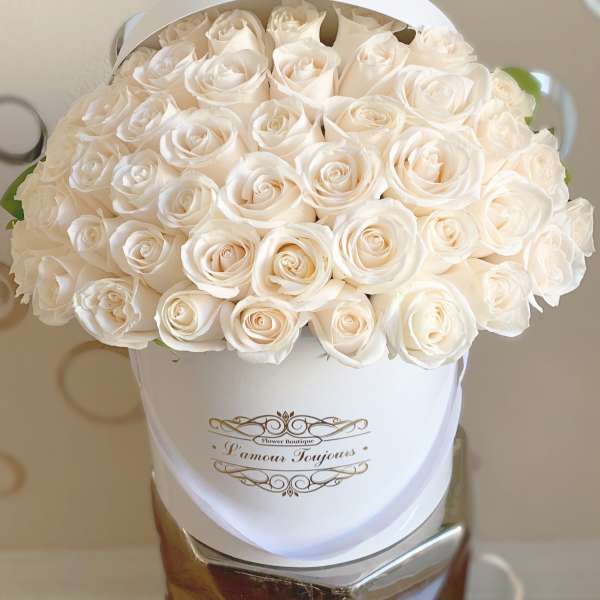 Round white hatbox filled with tightly packed ivory roses with gold script on the front