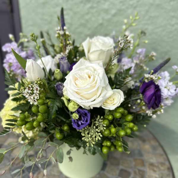 Arrangement of white roses and purple flowers in a light green vase on a mosaic table