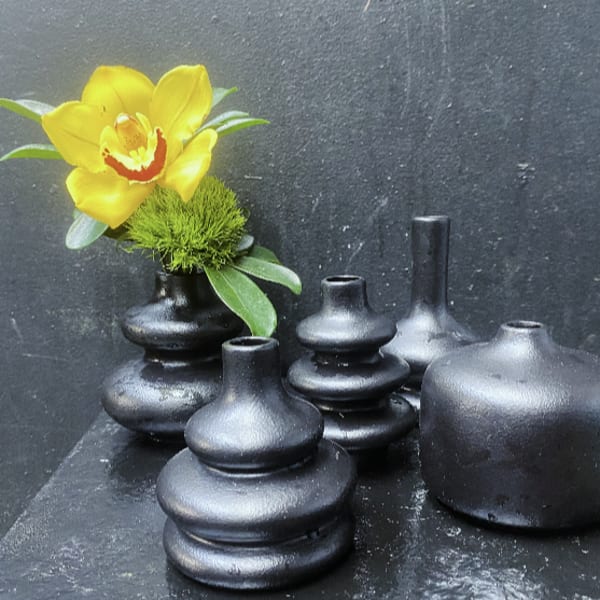 Yellow orchid in a small black vase with several black ceramic vases