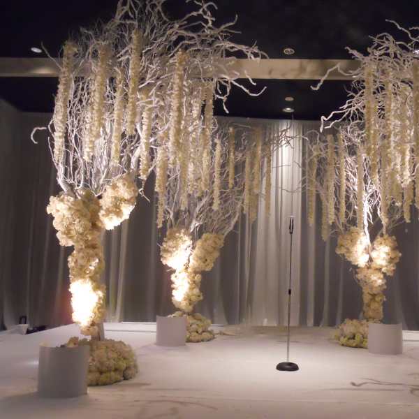 Tall white floral installations frame a stage with a microphone stand