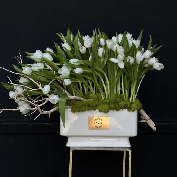 White tulips arranged in a white rectangular vase with moss and branches