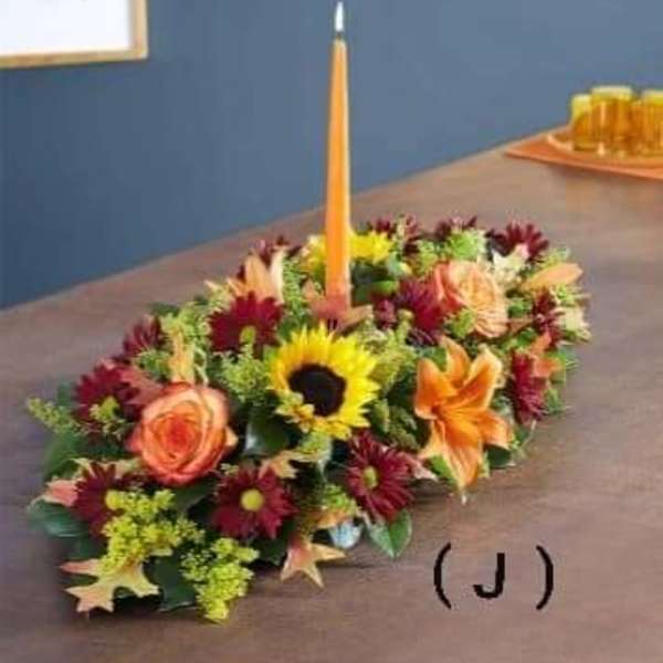 Low floral centerpiece with a tall orange taper candle