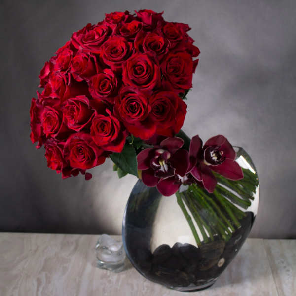 Red roses and dark orchids arranged in a clear glass vase