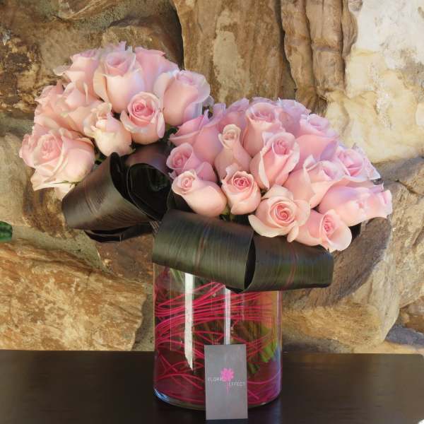 Two bouquets of pale pink roses in a glass vase with black ribbon