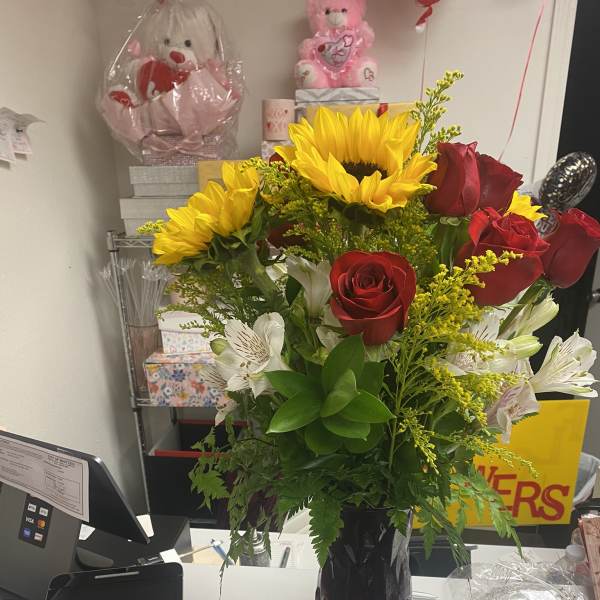 Bouquet of red roses, sunflowers, and white alstroemeria in a dark vase
