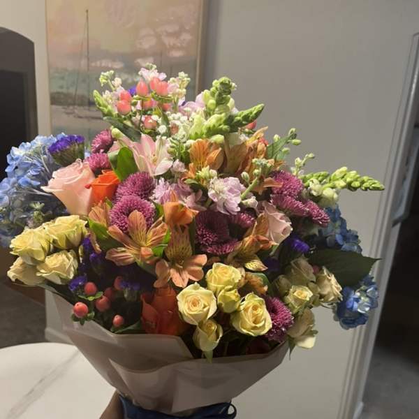 Mixed bouquet of colorful flowers wrapped in paper with a blue ribbon
