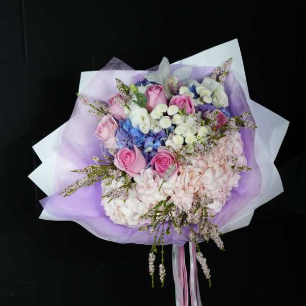 Bouquet of pink roses, hydrangeas, and white flowers wrapped in lavender paper