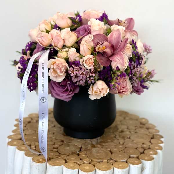 Pink and purple bouquet in a black vase with a ribbon