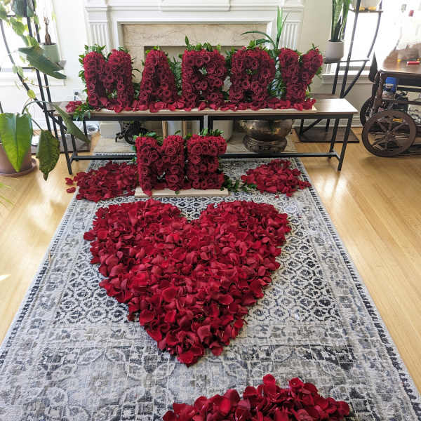 Red rose petals arranged in a heart shape with rose letter blocks on a table