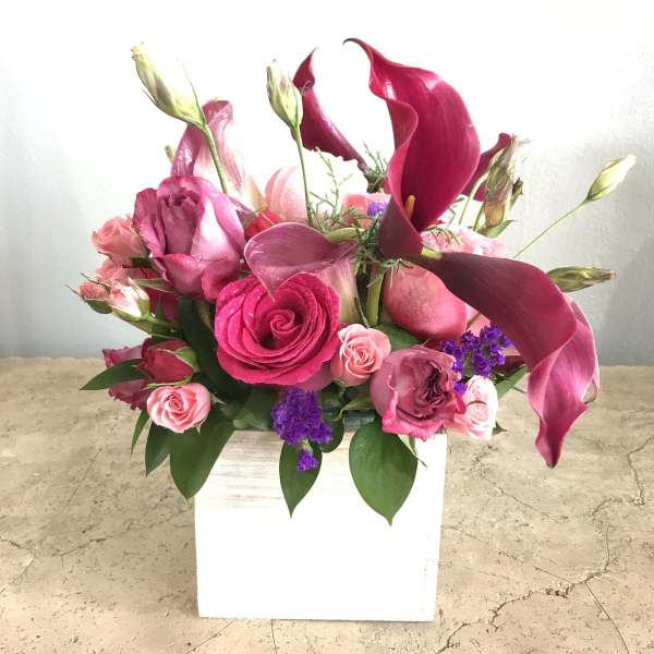 Pink and magenta floral arrangement in a white square vase