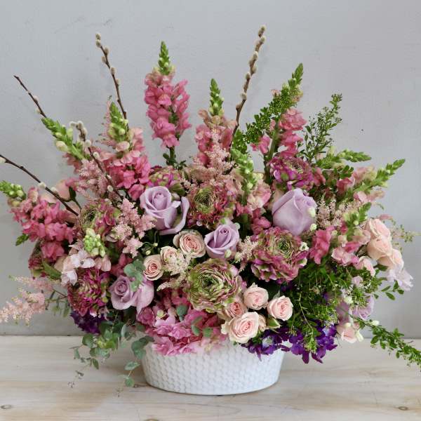 Lush pink and lavender flower arrangement with roses and snapdragons in a white ceramic bowl