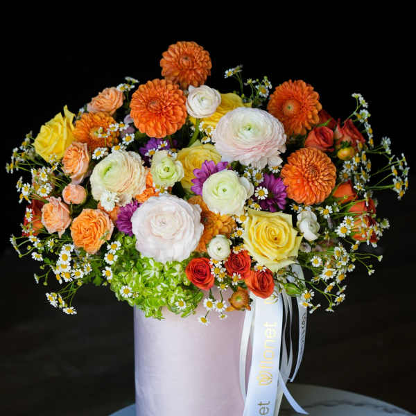Mixed bouquet of orange, yellow, white, and purple flowers in a pink hat box