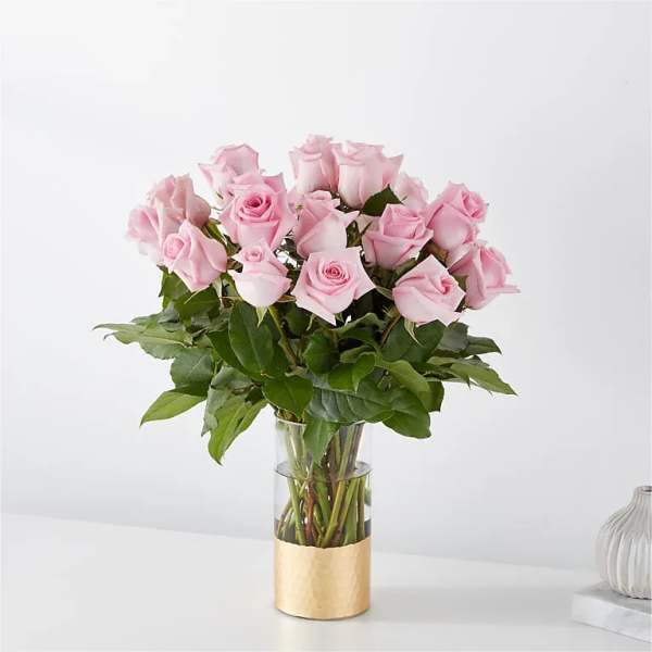 Pink roses arranged in a clear glass vase with a gold wrap