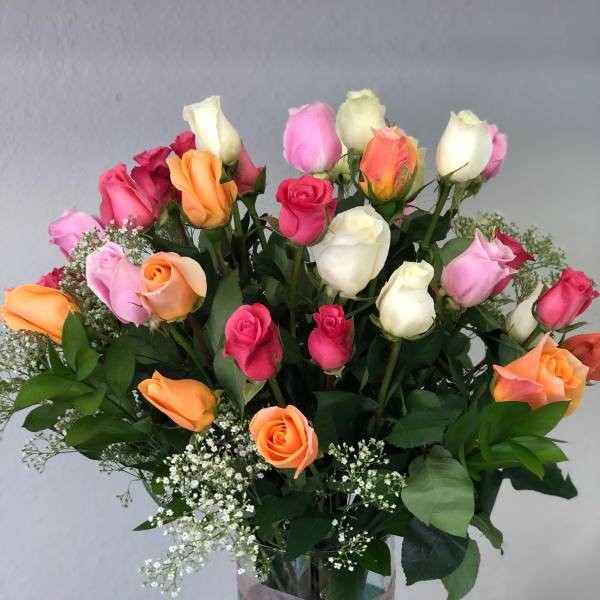 Mixed roses in pink, white, and orange arranged in a glass vase with a pink ribbon