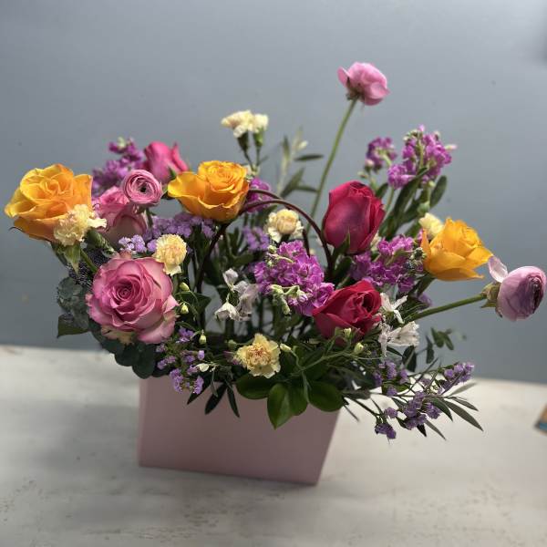 Mixed bouquet of pink, yellow, and purple flowers in a pink box