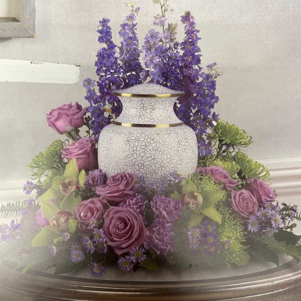 Purple roses and flowers arranged around a white urn on a table