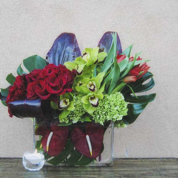 Red roses and green orchids arranged in a clear square vase