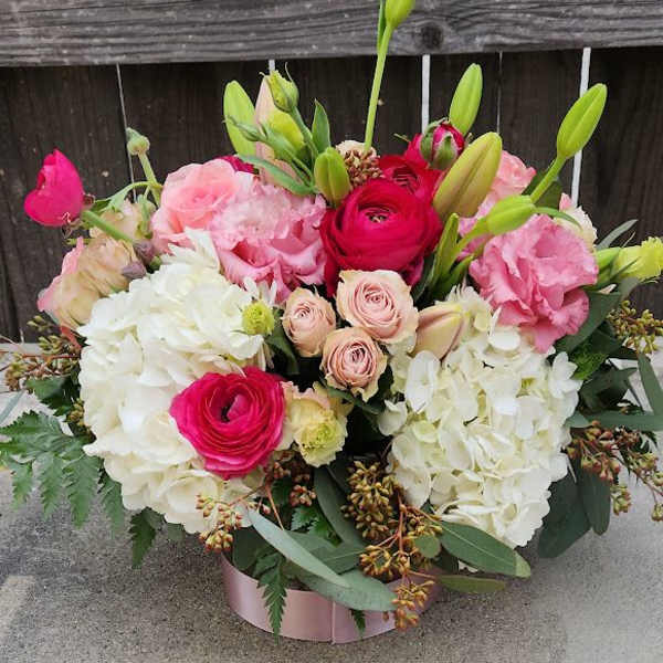 Low pink hatbox arrangement with white hydrangeas, pink spray roses, ranunculus, and lily buds