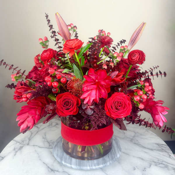 Red floral arrangement in a glass vase with a wide red ribbon