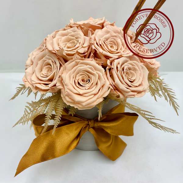 Bouquet of pale peach roses in a small vase with a gold ribbon