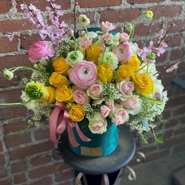 Bouquet of pink and yellow flowers in a teal hatbox with a pink ribbon
