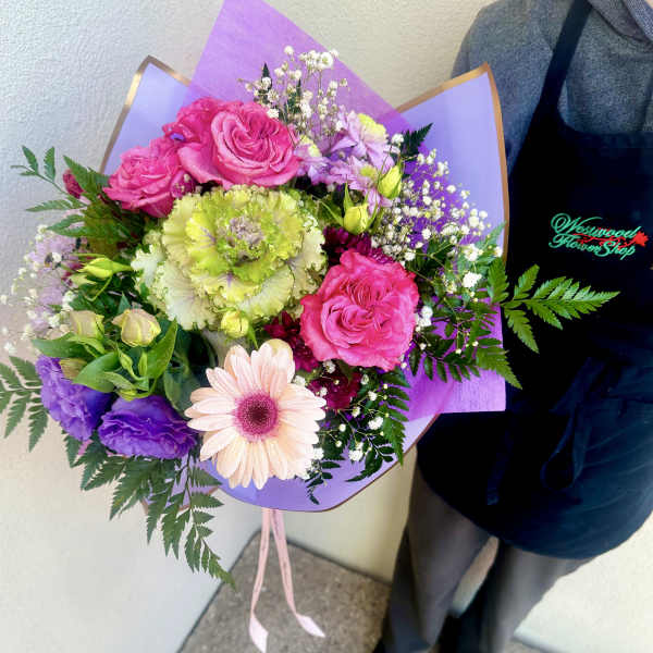 Bouquet of pink roses, a gerbera daisy, and purple flowers wrapped in lavender paper
