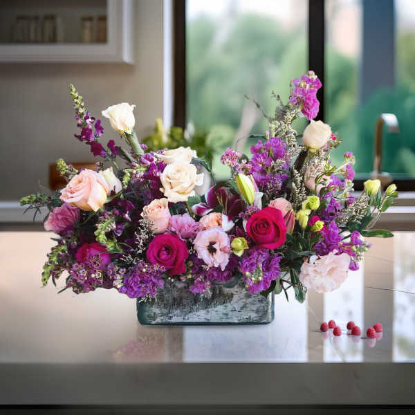 Mixed pink, purple, and white flower arrangement in a rectangular glass vase