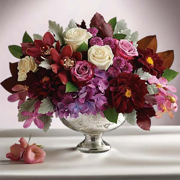Mixed bouquet of roses, orchids, and purple blooms in a silver pedestal vase