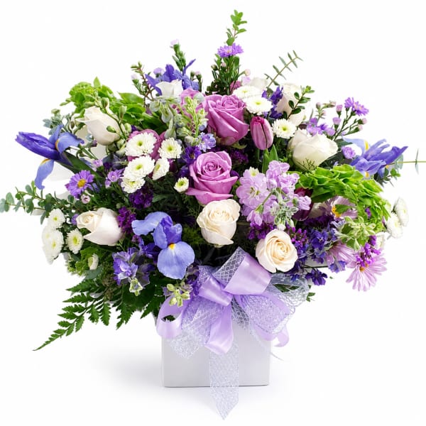 Lavender and white mixed flower arrangement in a square vase with a purple ribbon