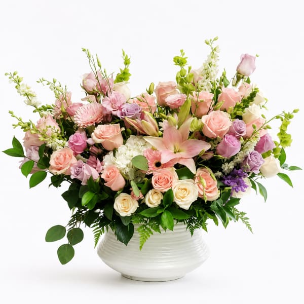 Pastel flower arrangement in a white vase with roses, lilies, and mixed blooms