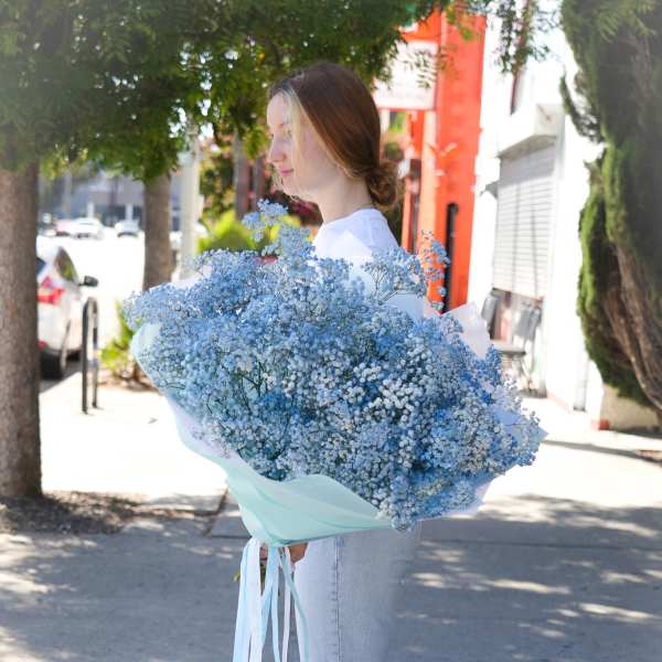 Woman holding a large bouquet of blue baby's breath wrapped in pale paper