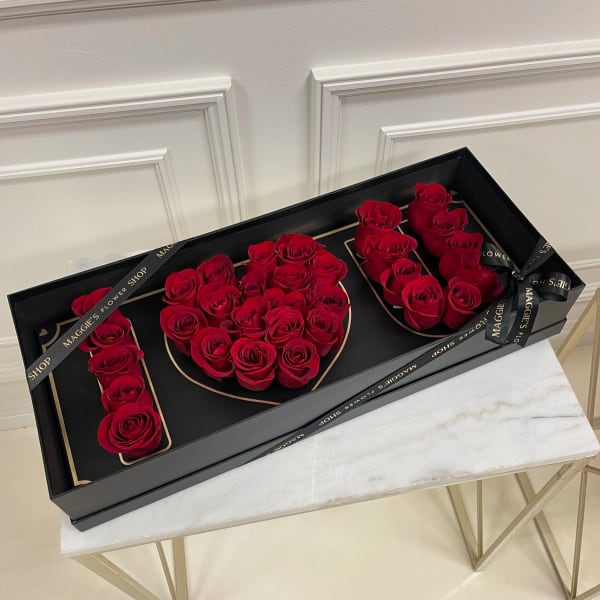 Red roses arranged in a black gift box spelling "LOVE"