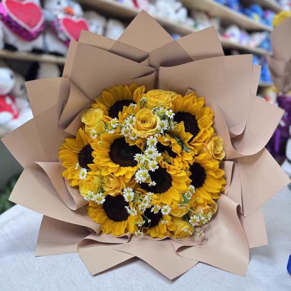 Bouquet of sunflowers, yellow roses, and small white daisies wrapped in tan paper