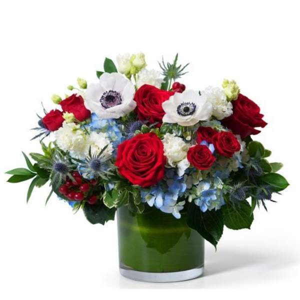 Red, white, and blue flower arrangement with roses and anemones in a green-lined glass cylinder vase