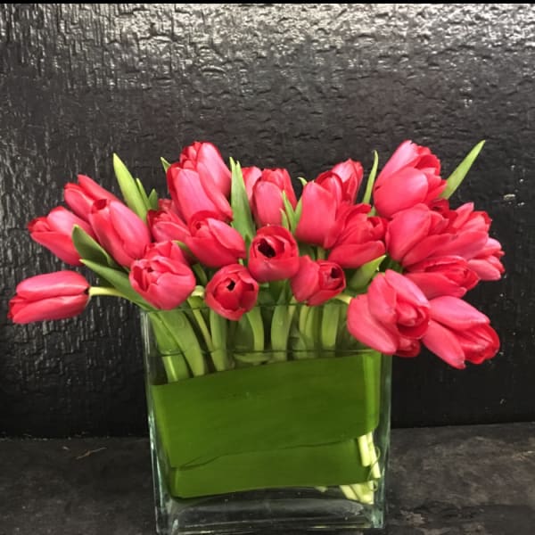 Pink tulips arranged in a clear glass vase with green wrap