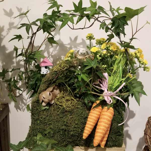 Moss-covered arrangement with yellow flowers, ivy, and two orange carrots