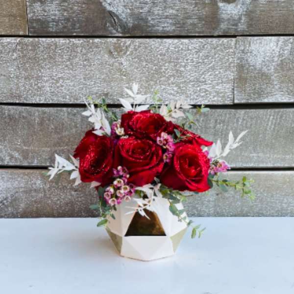 Red roses in a geometric white vase with small pink accents